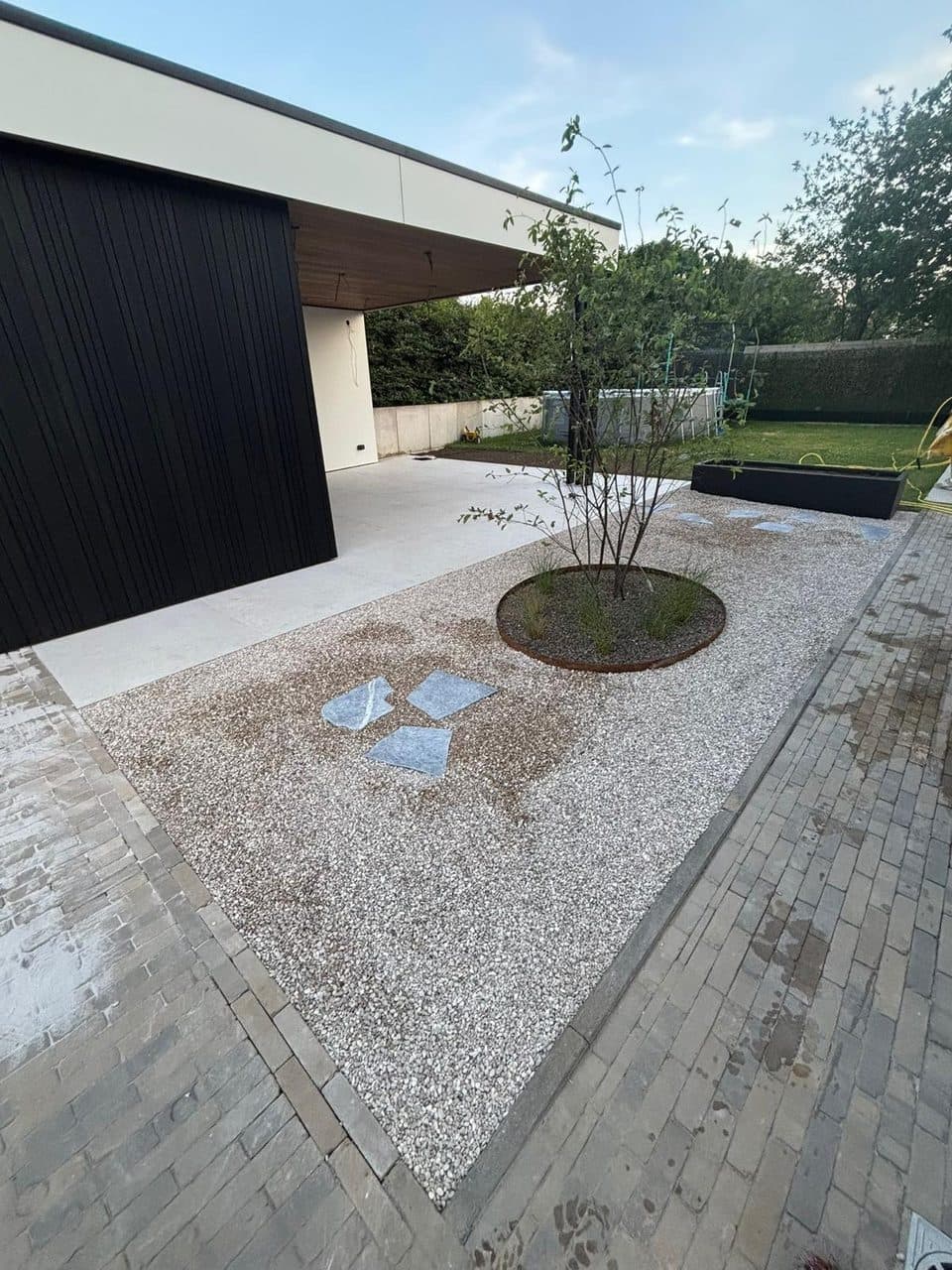 Aangelegd kiezeltuintje met natuurstenen stapstenen en ronde cortenstalen plantbak bij avondlicht